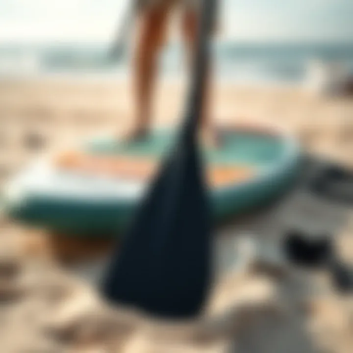 Close-up of paddleboarding equipment including a paddle and board on a sandy beach.